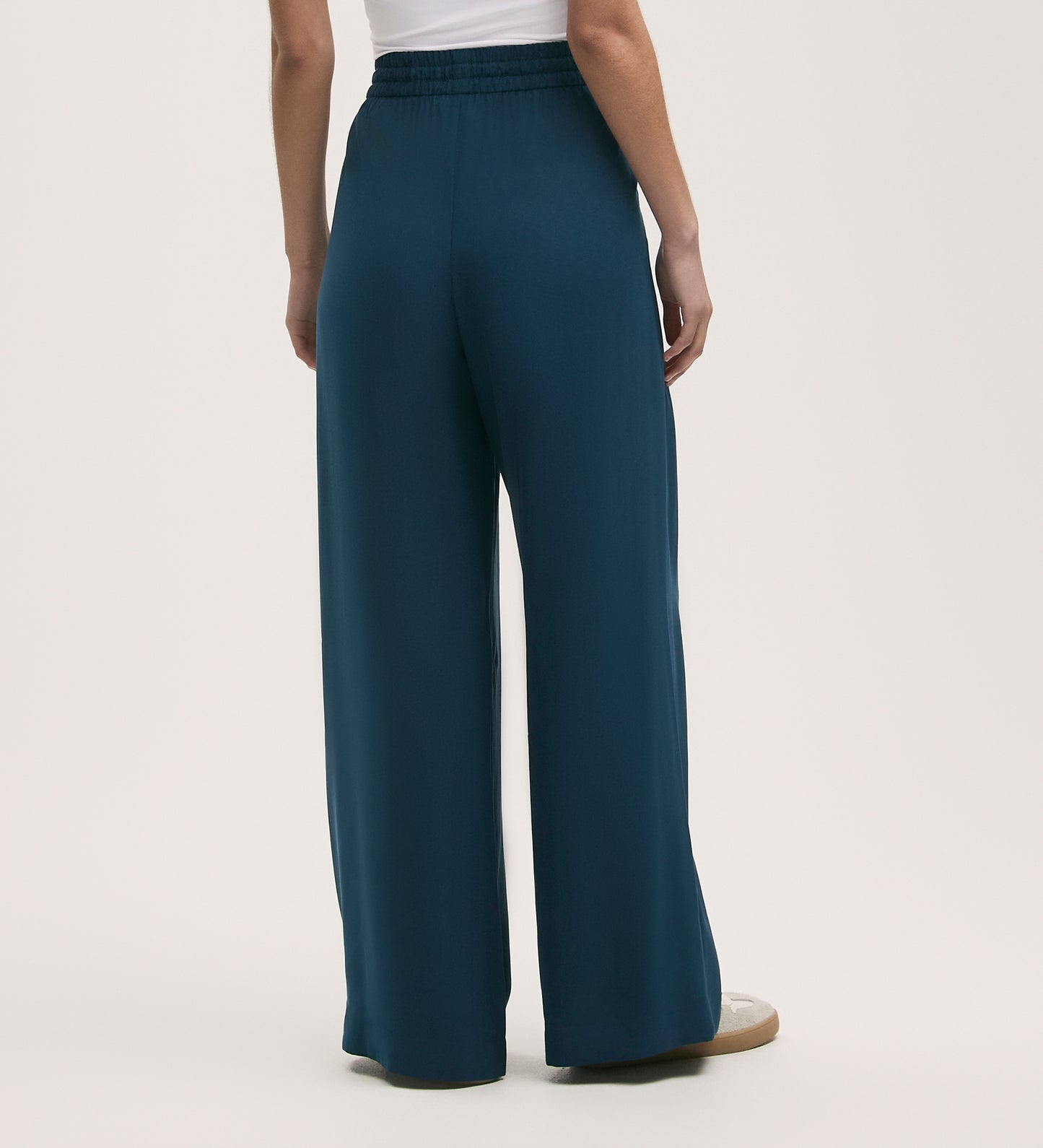 A person is shown from the waist down, wearing Dixie Indigo Wide Leg Trousers in teal with an elasticated waistband and a white top, standing against a plain background.