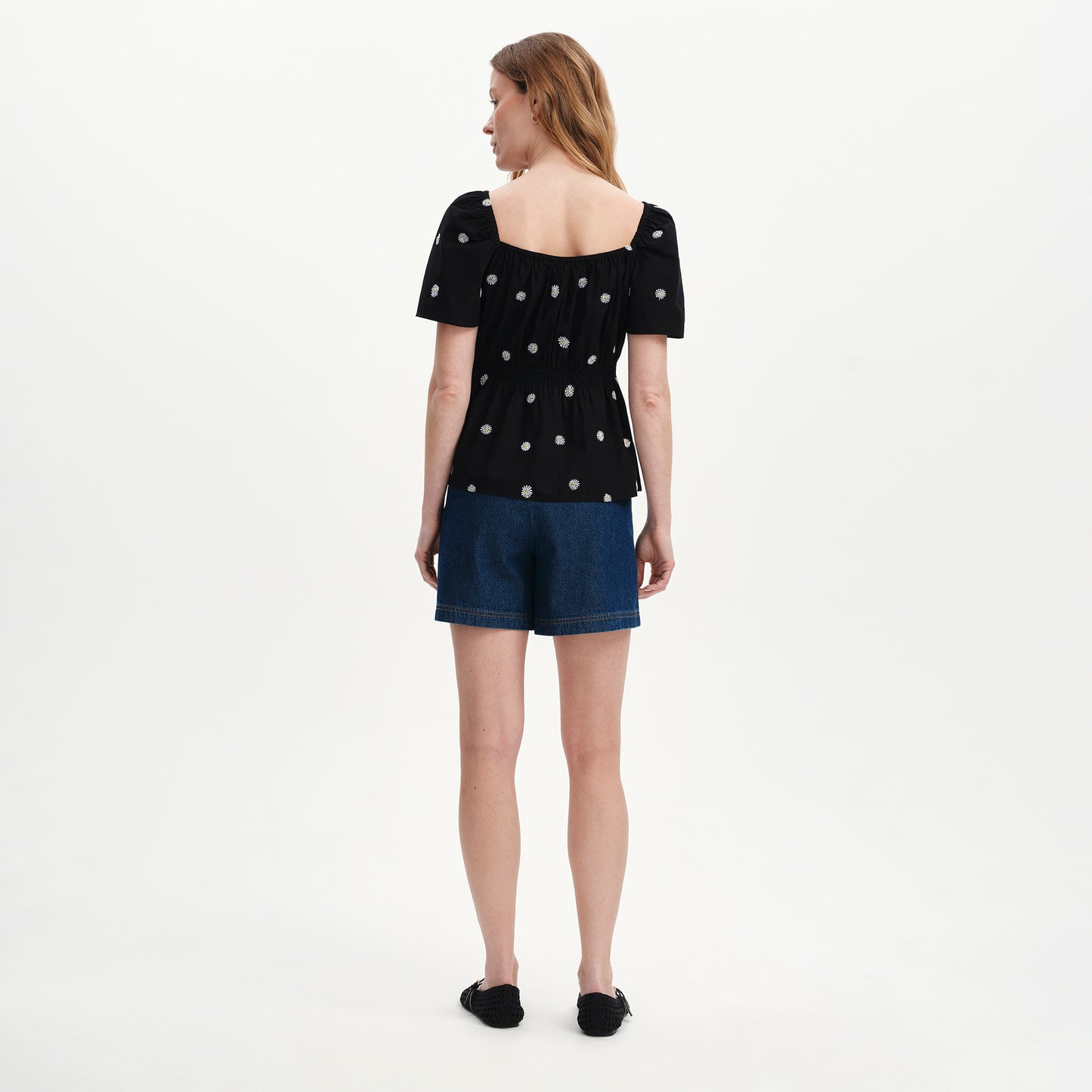 Woman wearing Holly Black Floral Embroidered Puff Sleeve Top and denim shorts on a white background