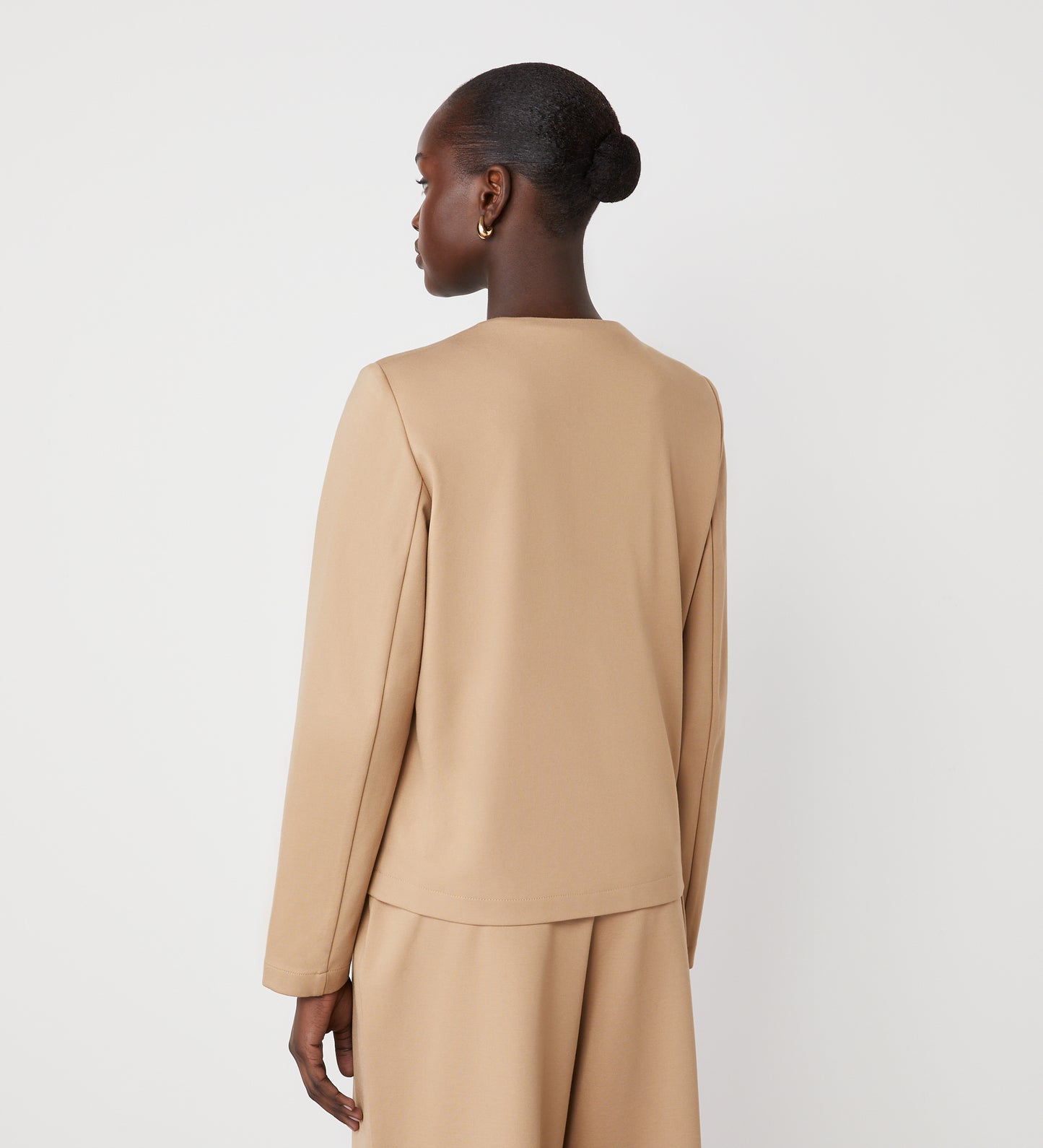 A person with short, dark hair in a bun models the Imogen Camel Ponte Jersey Jacket, shown from the back and slightly turned to the side against a plain white background.
