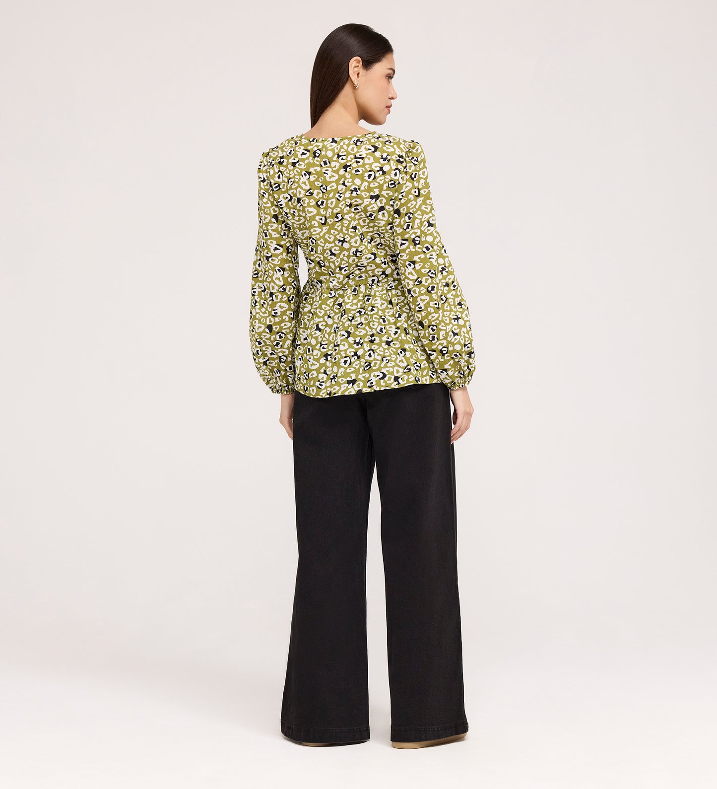 A woman faces away, wearing the Bel Green Leopard Cotton Blouse with long blouson sleeves and wide-leg black pants against a plain light background.
