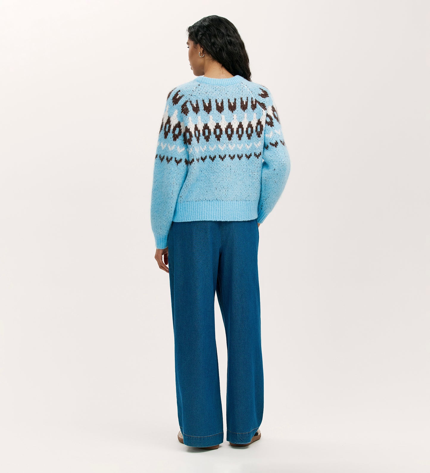 A person faces away, wearing the Belina Blue Knitted Jumper with a fair isle pattern and wide-leg blue pants—an ideal cozy winter look—set against a plain light background.