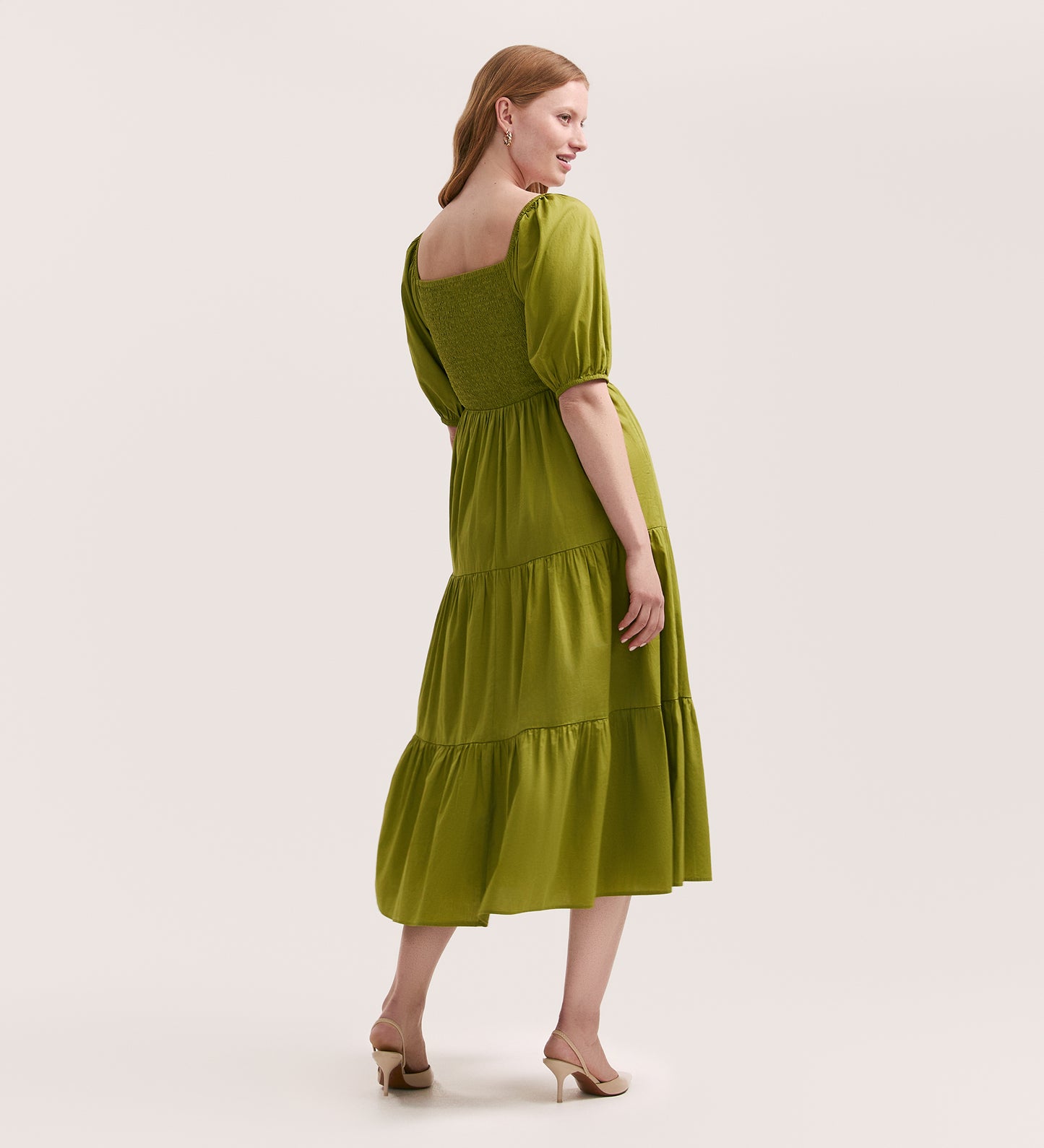 A woman poses in the Melody Light Green Cotton Midi Tiered Dress, featuring puff sleeves and a tiered skirt, standing in heels with a gentle smile against a neutral background.