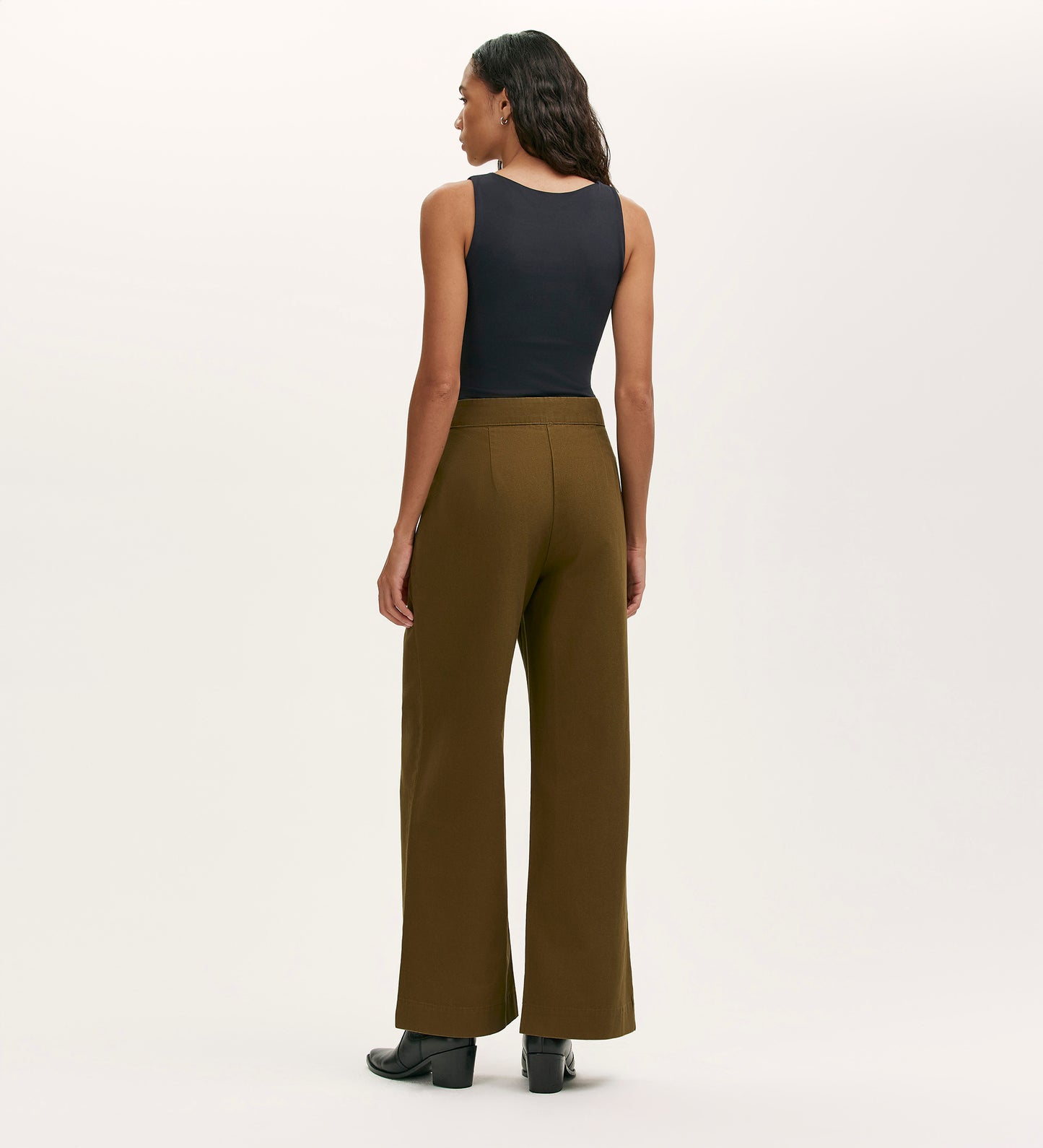 A woman stands facing away, wearing a sleeveless black top, the Nellie Khaki Canvas Wide Leg Trousers in olive green, and black shoes against a plain light background.