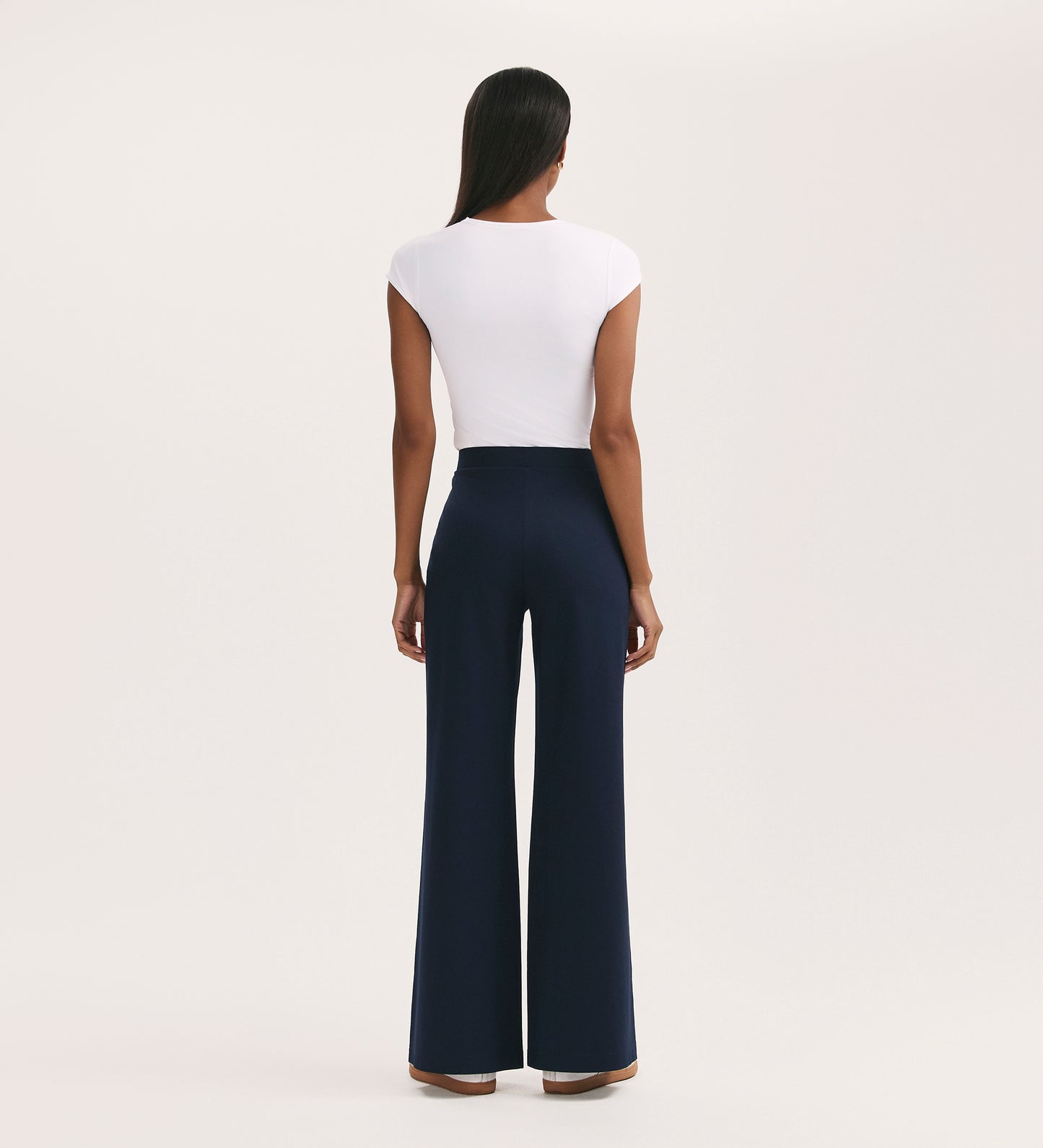 A person stands facing away against a plain light background, wearing a white short-sleeve top and Reyna Navy Ponte Jersey Wide Leg Trousers paired with brown shoes.