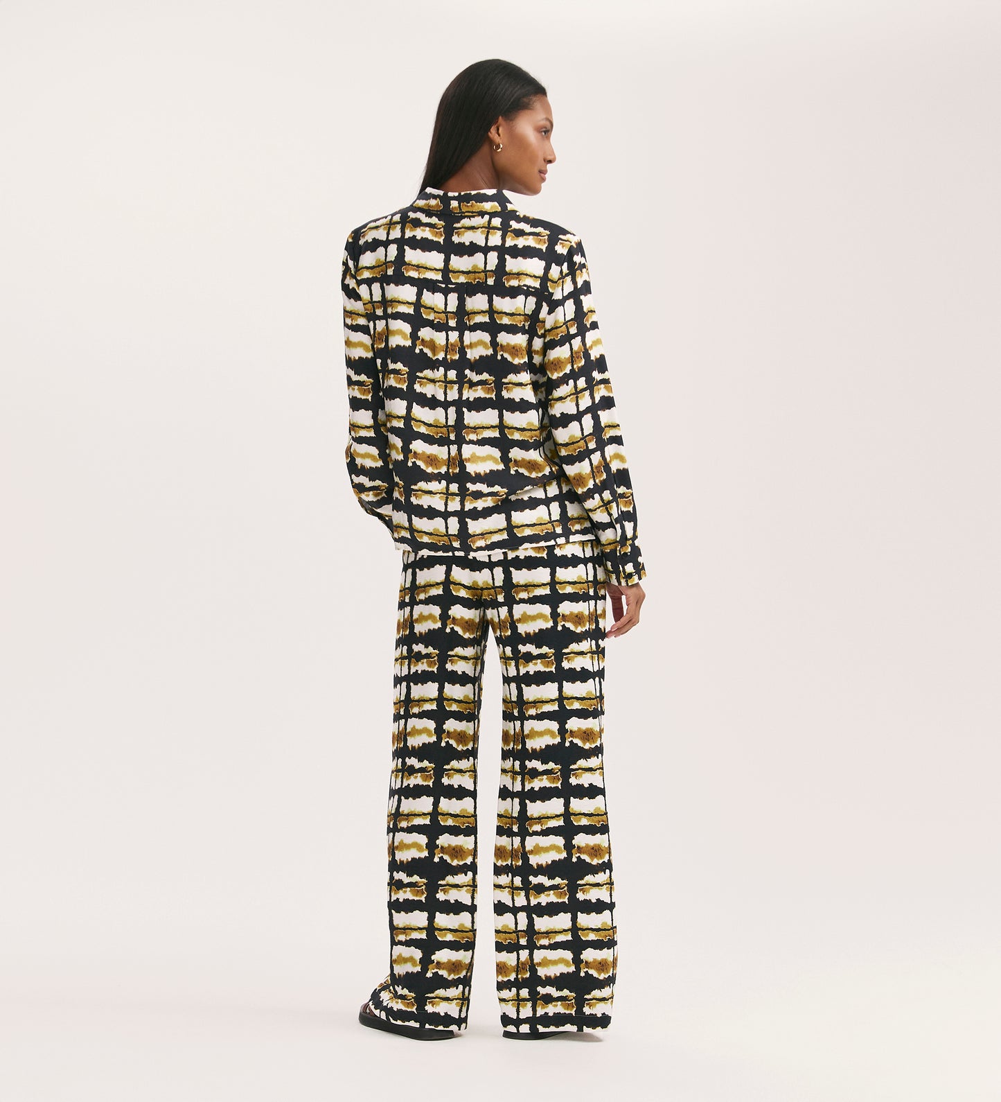 A woman faces away, wearing the Roma Black Tie Dye Crepe Button Through Shirt and wide-leg pants with a bold black, yellow, and white abstract print, creating a sophisticated look against a plain white background.