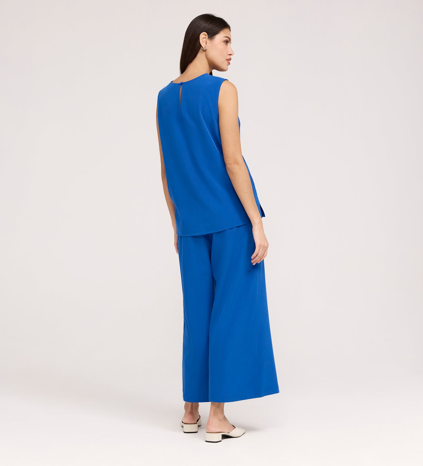 A woman with straight dark hair wears the Vallie Cobalt Round Neck Vest and matching relaxed wide-leg pants, paired with white shoes. She faces away from the camera against a plain, light background.