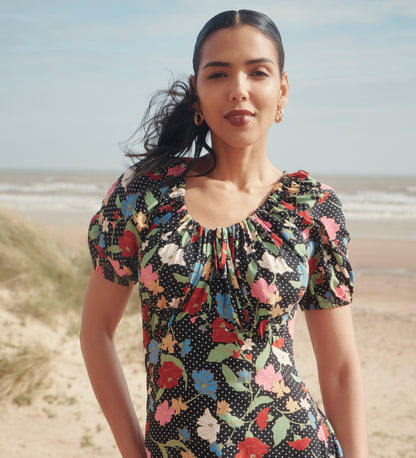 Woman wearing Jada Black Floral Puff Sleeve Empire Waist Midi Dress on a beach