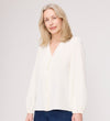 A woman with light blonde hair wears the Elvora Ivory Button Up V-neck Top and blue pants, standing against a plain light background while smiling softly at the camera.