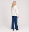 A woman with blonde hair wears the Elvora Ivory Button Up V-neck Top, paired with long sleeves, wide-leg blue jeans, and black heels, standing and facing away from the camera against a plain light background.