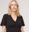 A woman with shoulder-length blonde hair wears the Maryam Black Button Up V-Neck Short Sleeve Top, standing against a plain light background and looking at the camera with a neutral expression.