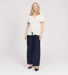 A woman with light blond hair wears the Maryam Ivory Button Up V-Neck Short Sleeve Top, paired with dark wide-leg jeans and black heels, standing facing forward against a plain white background.