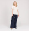 A woman with light hair wears the Maryam Ivory Button Up V-Neck Short Sleeve Top with dark wide-leg pants and black heels, standing against a plain light background. Her expression is relaxed and neutral.