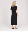 A woman with blonde hair, wearing the Priscilla Black Cupro Midi Dress and black heels, stands facing away from the camera against a plain light background.