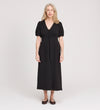 A woman with long, light hair stands facing forward in the Robyn Black Button Through Midi Dress with short sleeves and flat shoes, against a plain, light background. Ideal as a versatile day to evening dress for any occasion.
