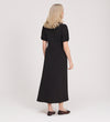 A woman with blonde hair faces away, wearing the Robyn Black Button Through Midi Dress with puff sleeves and black flats, set against a plain light background.