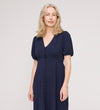 A woman with shoulder-length blonde hair wears the Robyn Navy Button Through Midi Dress with short puff sleeves and an empire waist, standing against a plain light background and smiling softly at the camera.