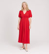 A woman with light blonde hair smiles softly as she stands against a plain white background, wearing the Robyn Red Button Through Midi Dress with short sleeves and white flats.
