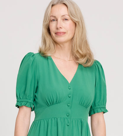 A woman with wavy blonde hair, smiling gently, wears the Samantha Green Button Through Midi Dress with a V-neckline and short puff sleeves, standing against a plain light background.