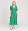 A woman with long, light hair wears the Samantha Green Button Through Midi Dress, featuring puff sleeves and a V-neckline, paired with white sneakers, standing against a plain white background.