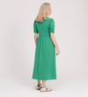 A woman with blonde hair stands facing away, wearing the Samantha Green Button Through Midi Dress and white sneakers with green accents against a plain light background.