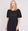 A woman with light blonde hair smiles gently at the camera, wearing the Yasmine Black Jersey Midi Dress against a plain light background.