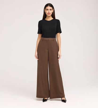 A woman stands against a plain background, wearing a black short-sleeve top, black pointed-toe shoes, and the Addie Mushroom Gaberdine Twill Wide Leg Trousers. She faces forward with a neutral expression and her arms at her sides.