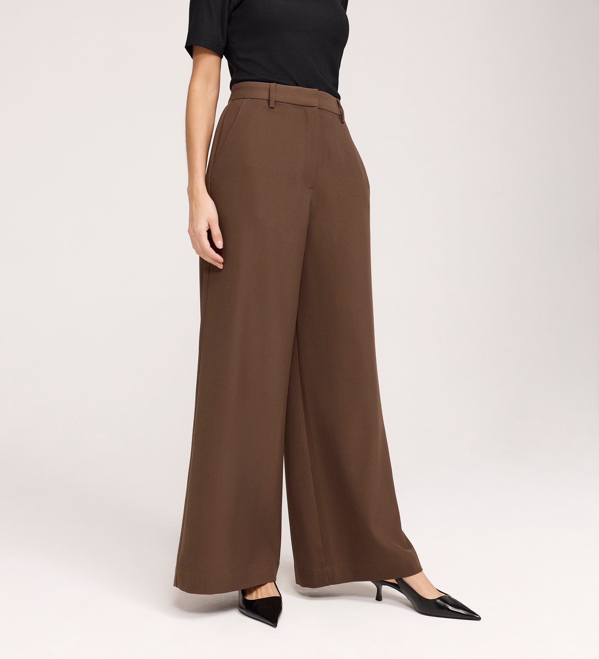 A person wearing a black short-sleeve top, Addie Mushroom Gaberdine Twill Wide Leg Trousers, and black pointed-toe heels stands against a plain light background.