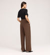 A woman stands with her back to the camera, wearing a black short-sleeve top and the Addie Mushroom Gaberdine Twill Wide Leg Trousers, hands in pockets, against a plain light background.