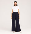 A woman faces forward against a plain light background, wearing a white short-sleeve t-shirt, the Addie Navy Gaberdine Twill Wide Leg Trousers, and white shoes.