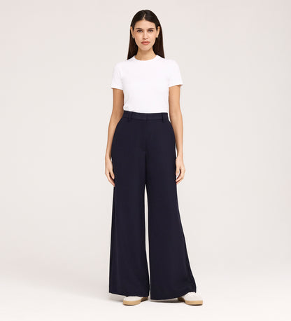 A woman faces forward against a plain light background, wearing a white short-sleeve t-shirt, the Addie Navy Gaberdine Twill Wide Leg Trousers, and white shoes.