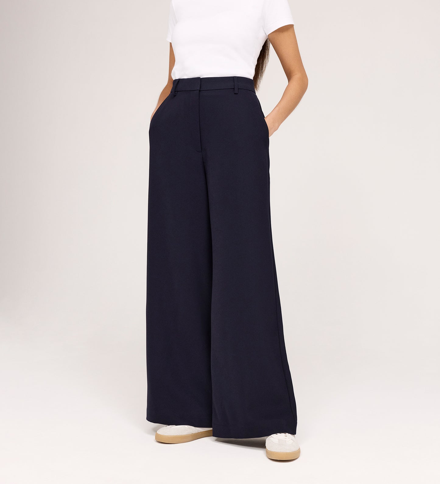 Only the lower half of a person is visible, wearing a white short-sleeve top and Addie Navy Gaberdine Twill Wide Leg Trousers with hands in pockets, standing against a white background.