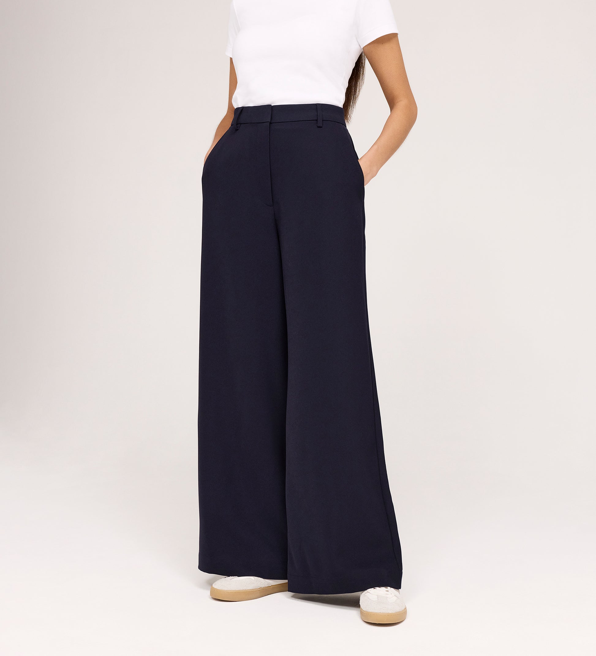 Only the lower half of a person is visible, wearing a white short-sleeve top and Addie Navy Gaberdine Twill Wide Leg Trousers with hands in pockets, standing against a white background.