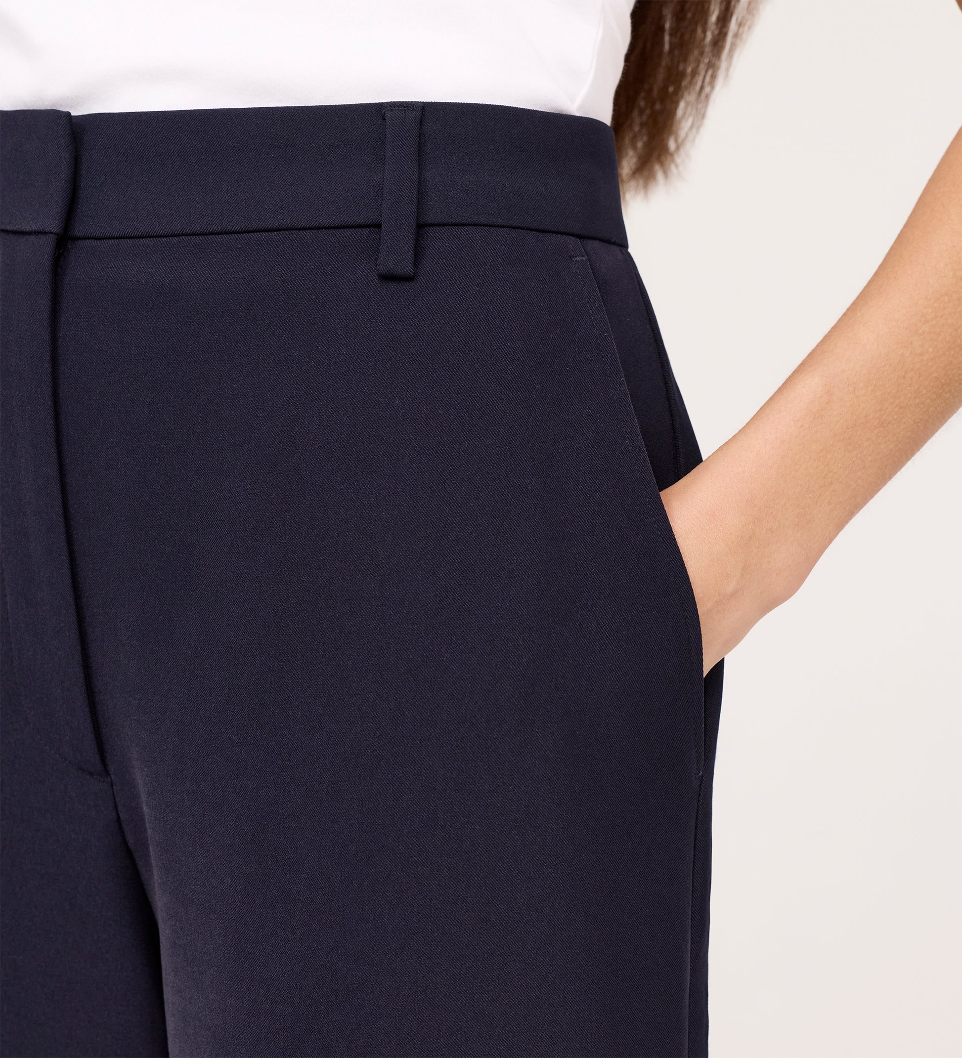 A person models the Addie Navy Gaberdine Twill Wide Leg Trousers with a white top, right hand in the pocket, shown from the waist down against a plain background.