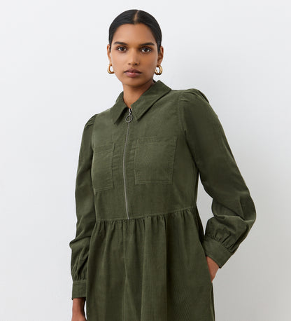 A woman confidently stands against a plain white background wearing the Callie Khaki Corduroy Midi Dress, featuring chest pockets and a front zipper.