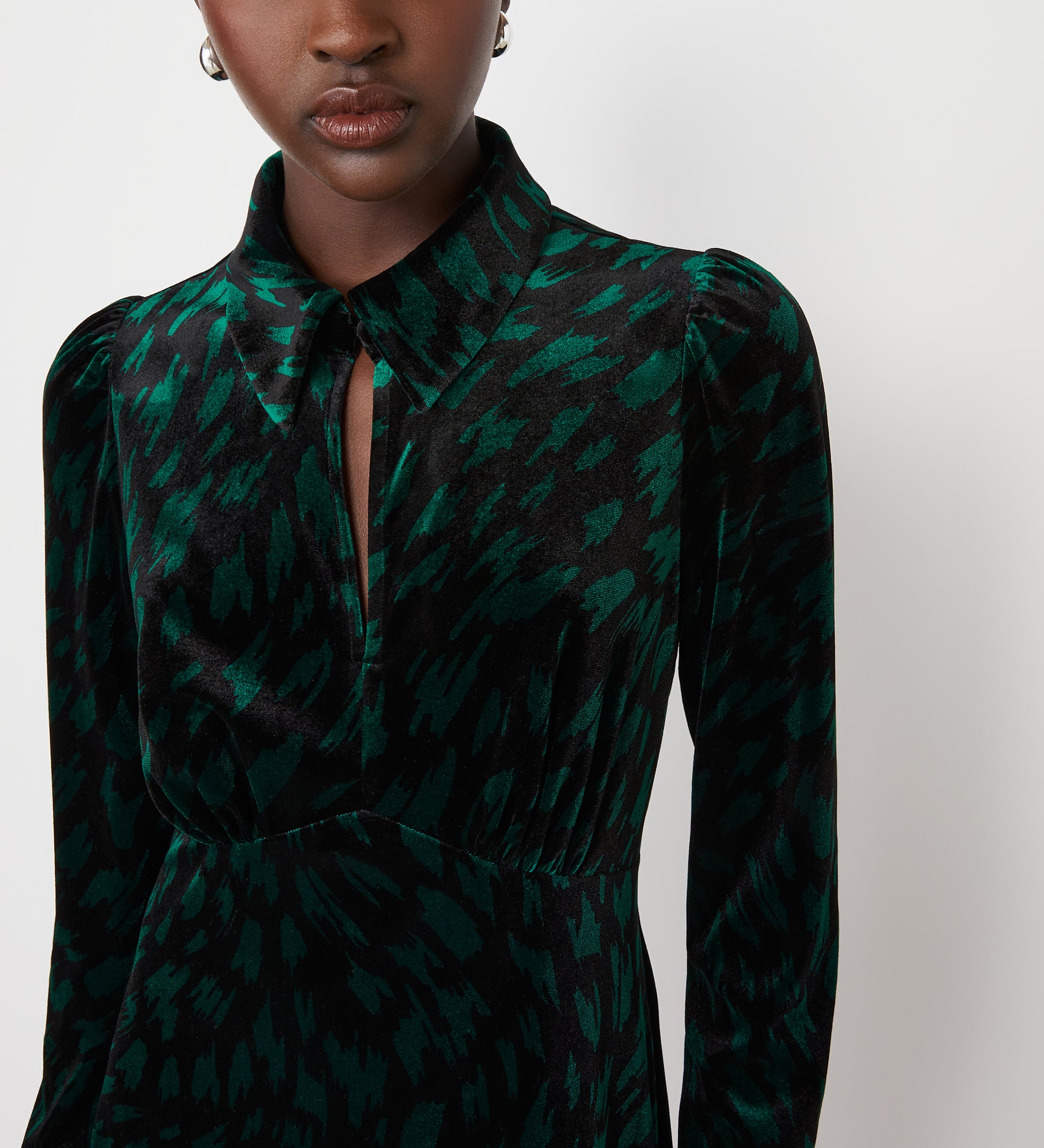 A woman wears the Capri Green Animal Knee Length Dress—a dark green and black patterned velvet dress with long sleeves, pointed collar, empire waist, and keyhole cutout—perfect for parties. The background is plain white.