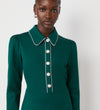 A woman stands against a plain light background wearing the Clarice Bottle Green Ponte Jersey Midi Dress, featuring long sleeves, pearl-like buttons on the functional placket, and white trim along the collar and placket.