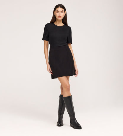 A woman stands against a plain background, wearing the Cherry Black Short Sleeve Jersey T-Shirt with a relaxed fit, paired with a black mini skirt and knee-high black boots.