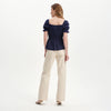 Woman wearing Cynthia Navy Gingham Seersucker Shirred Puff Sleeve Top and beige pants on a white background