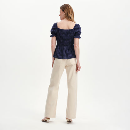 Woman wearing Cynthia Navy Gingham Seersucker Shirred Puff Sleeve Top and beige pants on a white background