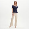 Woman wearing Cynthia Navy Gingham Seersucker Shirred Puff Sleeve Top and beige pants on a white background