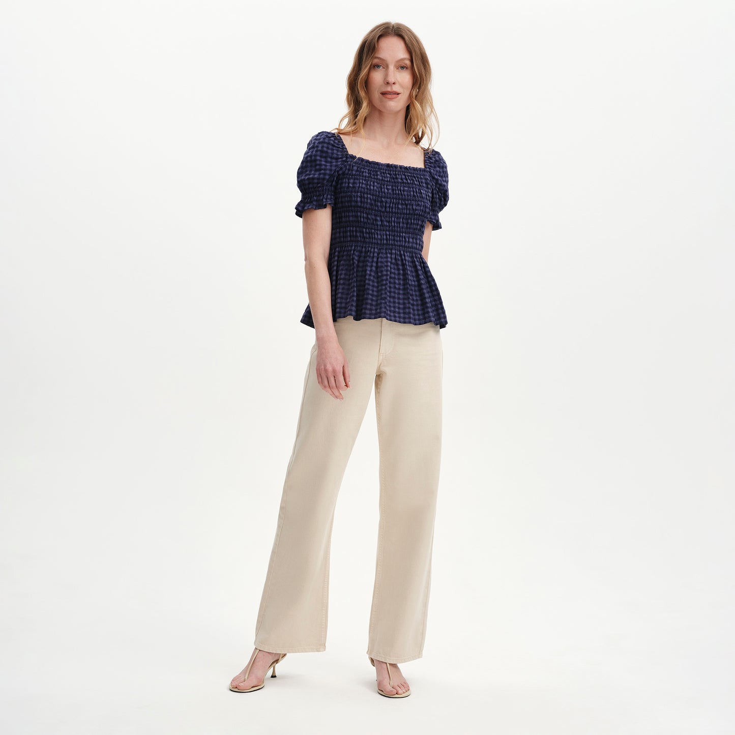 Woman wearing Cynthia Navy Gingham Seersucker Shirred Puff Sleeve Top and beige pants on a white background