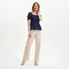 Woman wearing Cynthia Navy Gingham Seersucker Shirred Puff Sleeve Top and beige pants on a white background