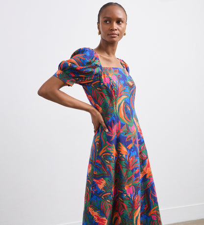 A woman poses against a white background wearing the Daisy Green Tropical Linen Blend Midi Dress, featuring a colorful tropical print, puffed short sleeves, and a square neckline—ideal as a chic summer dress for warm days.