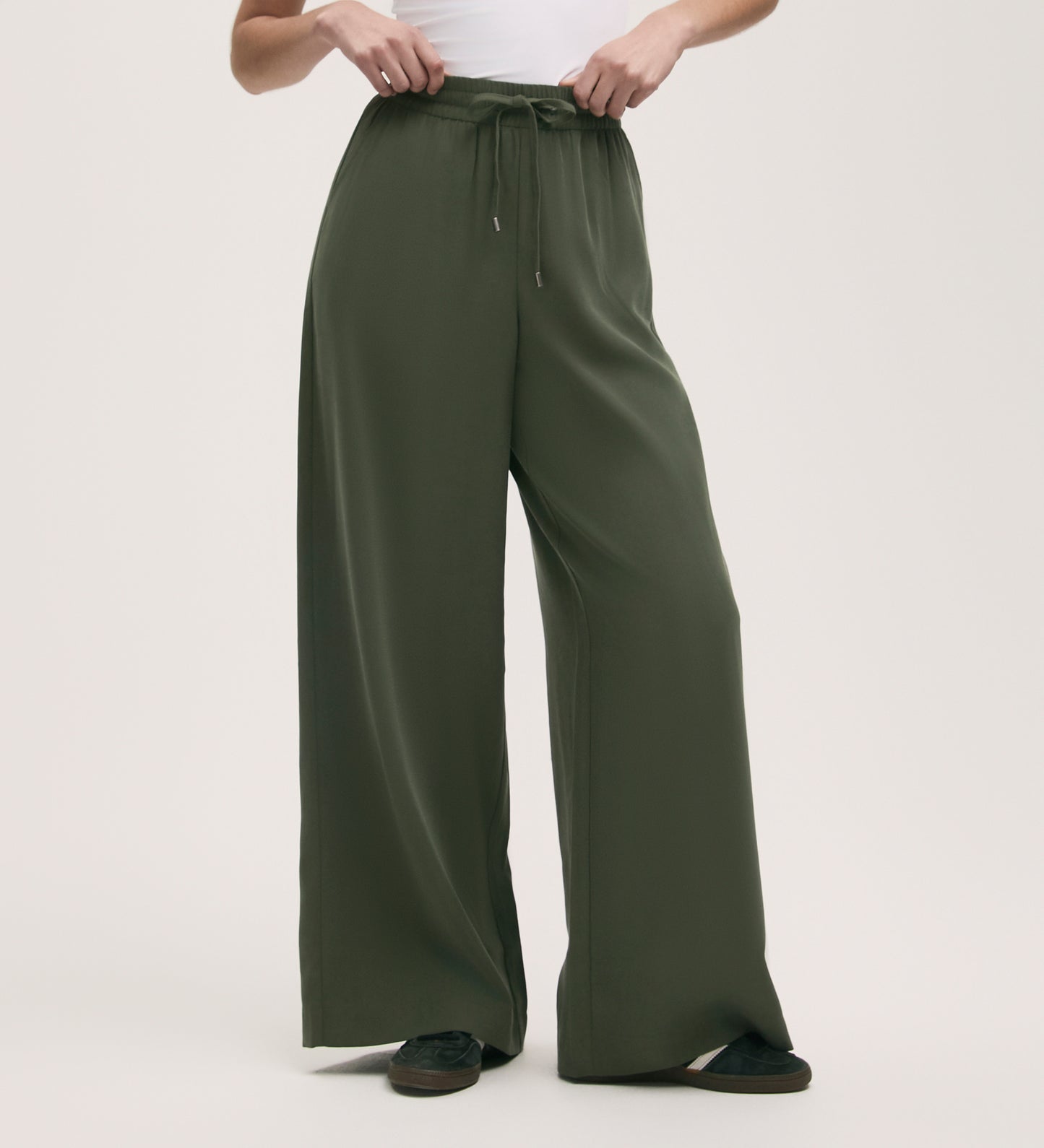 Wearing Dixie Khaki Wide Leg Trousers with a relaxed fit and elasticated waistband, paired with a white top and black shoes, the person stands against a plain light background.