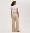 A woman with curly hair stands facing away against a light background, wearing a white short-sleeve fitted top and Dixie Stone Wide Leg Trousers featuring a relaxed fit and elasticated waistband.