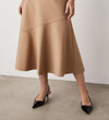 Model showcases the Grace Camel Ponte Jersey Midi Skirt—an effortlessly classic, tan, knee-length skirt—standing on a concrete floor against a plain white wall, with only the lower half of their body visible.