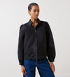 A woman wears the Jayne Black Broderie Cotton Shirt, featuring blouson sleeves and eyelet hem detailing, paired with blue jeans. She stands against a plain white background.