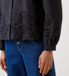 Wearing the Jayne Black Broderie Cotton Shirt featuring blouson sleeves, intricate lace embroidery on the hem and cuffs, and a floral cutout pattern, paired with blue jeans.