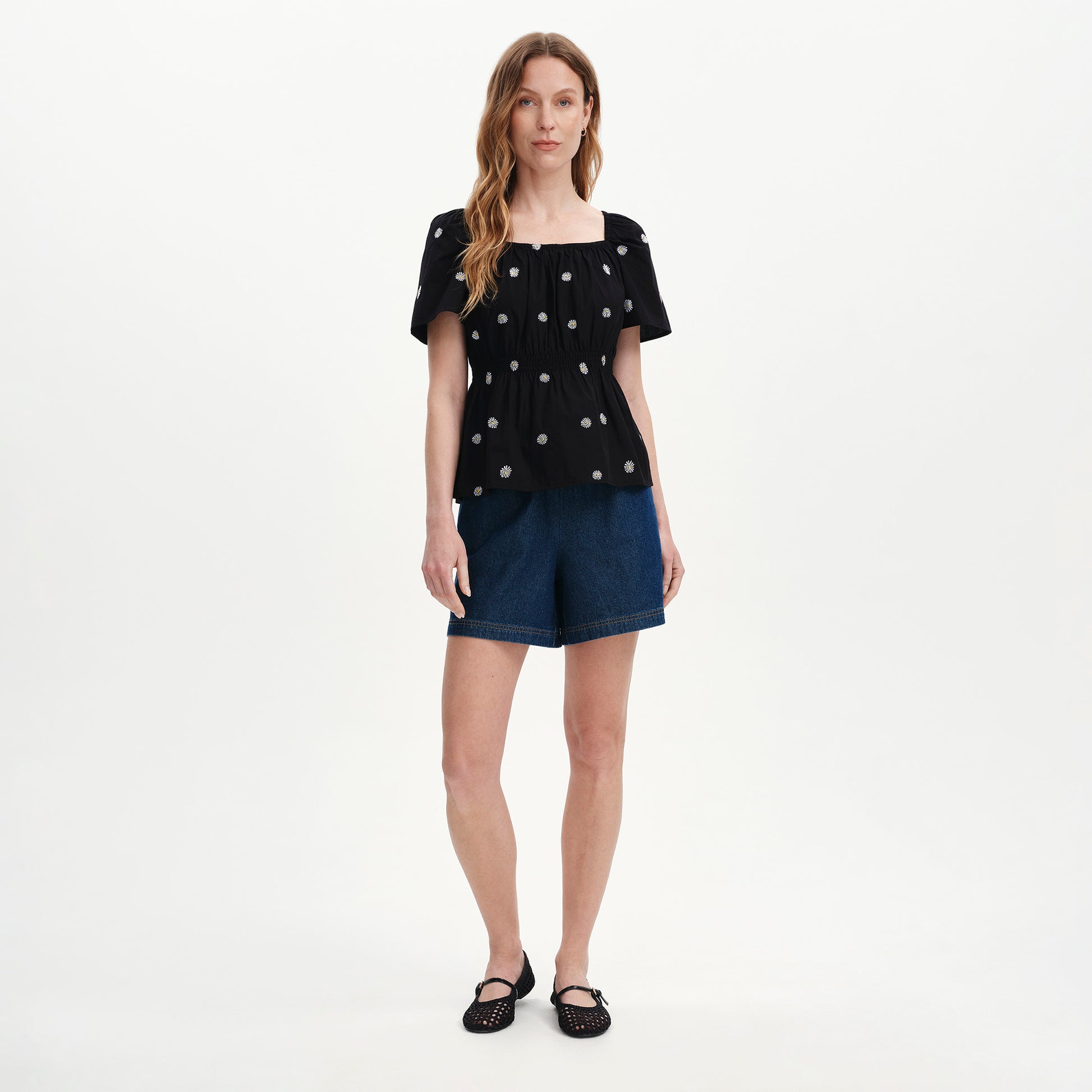 Woman wearing Holly Black Floral Embroidered Puff Sleeve Tops and denim shorts on a white background