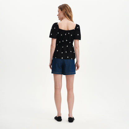 Woman wearing Holly Black Floral Embroidered Puff Sleeve Top and denim shorts on a white background